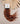 Wavy extension hair in a coffee brown ombre color with warm coppery highlights, attached to a white and black brand card, styled with dried palm leaves on a neutral beige background.